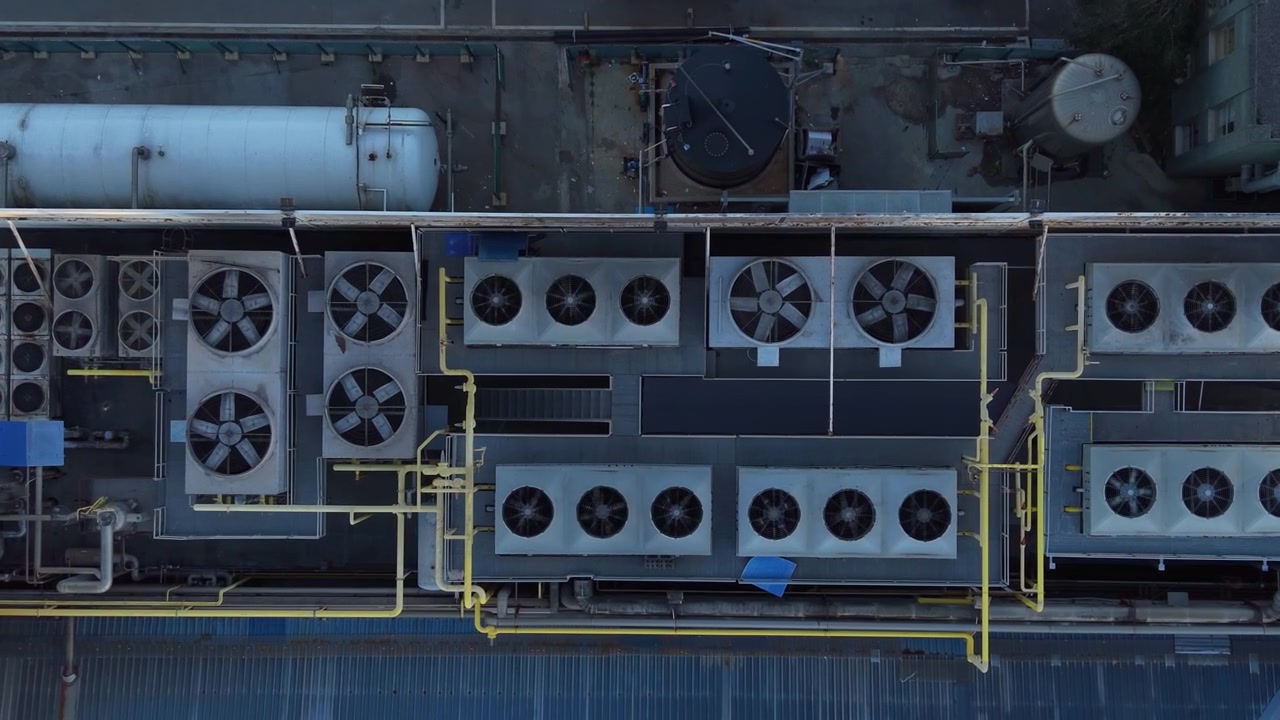 Top-down view of industrial rooftop HVAC units with large cooling fans, yellow pipework and pressure tanks on a factory or commercial building