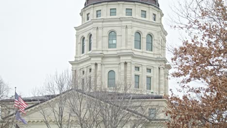 kansas state capitol building with flags waving in topeka, kansas with medium shot video tilting down from dome in slow motion