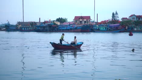 wideshot of two people in a rowboat in a small vietnamese fishing village