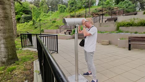 Woman-looks-through-observation-telescope-at-scenic-lookout-point