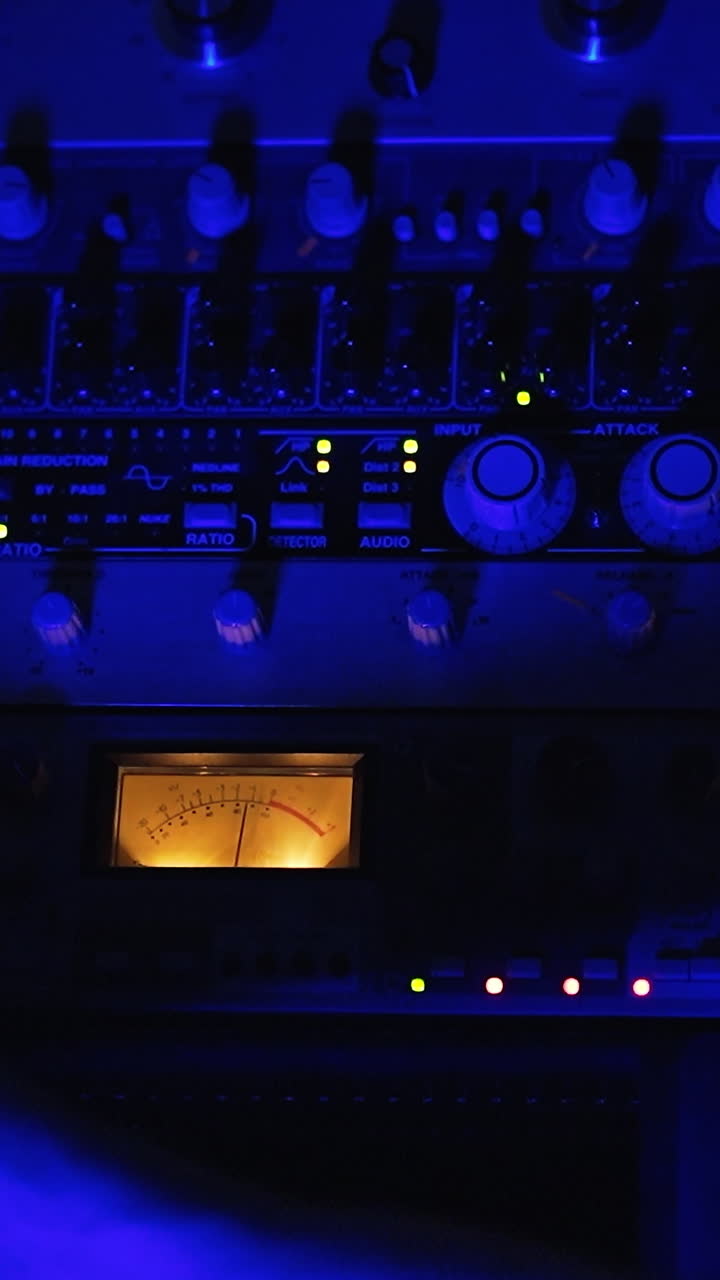 Studio recording equipment in the blue light. Male audio engineer's hand working on the stereo panel. Top view close up. Vertical video