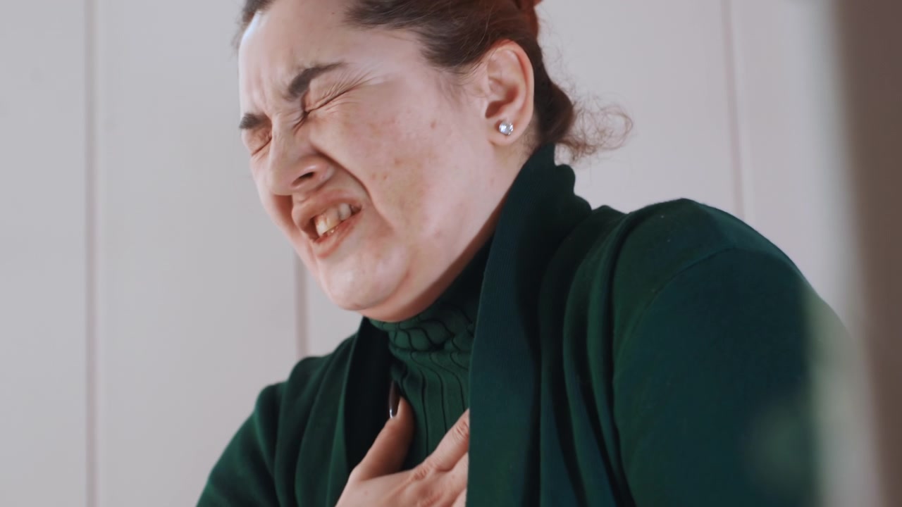 Woman experiencing intense chest tightness at home closeup, painful grimace and clutching hand over heart, visible shortness of breath and anxiety, emotional and medical urgency in quiet interior