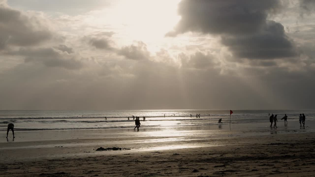 grey Bali beachfront with sun shining through clouds with silhouettes of people timelapse
