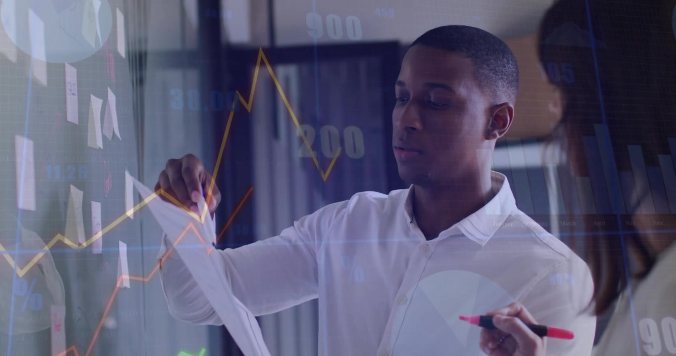 Analyst checking paper, pointing and writing on glass with Post-its, rising finance charts guiding