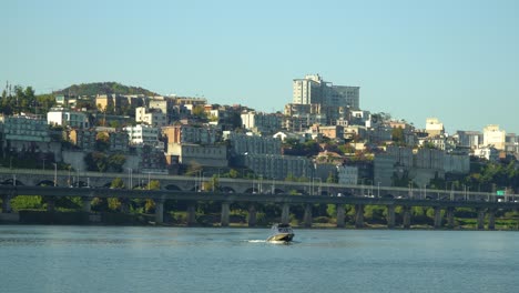 motorboat traveling across hangang or han river with yongsan-gu district skyline and gangbyeon expressway on background on a cloudless autumn day, seoul, south korea