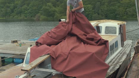 lifting waterproof canvas cover over rooves of wooden boat