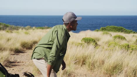 african american man exercising outdoors sitting on a rock in countryside on a coast