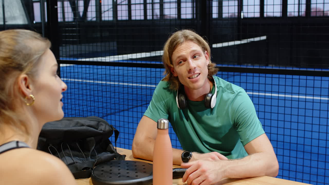 Ung mann med hodetelefoner diskuterer padelstrategi på en innendørsbane.