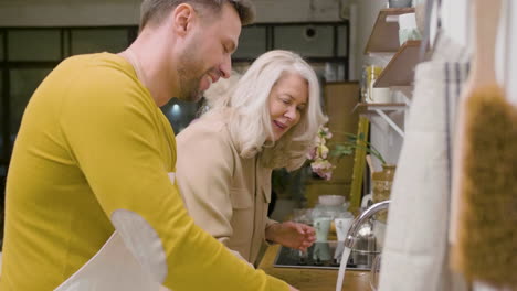 side view of a man washing the family dinner dishes at the sink in the kitchen while a mature woman helping him 1