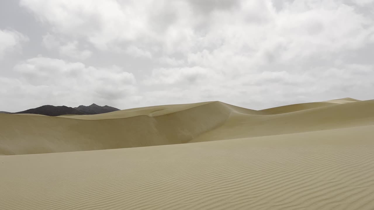 Breathtaking panorama of the Viana Desert's undulating sand dunes on Boa Vista, Cape Verde. The scene is framed by an overcast sky, emphasizing the stark beauty of this remote and unspoiled landscape