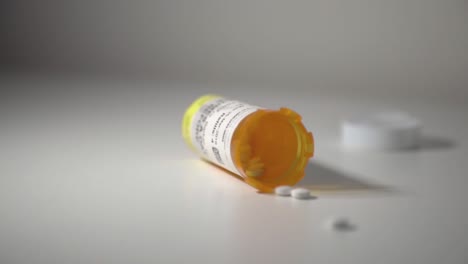 White-Pills-Spilling-Out-Of-A-Toppled-Yellow-Pill-Bottle-On-Top-Of-A-White-Table