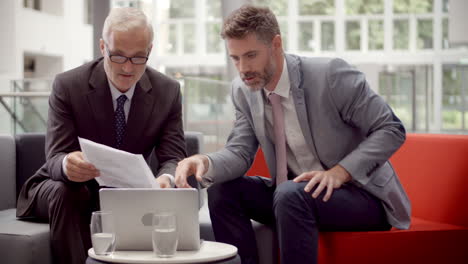 two businessmen discuss document in lobby of modern office