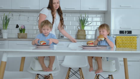 two kids in blue shirts eating burgers in the bright kitchen