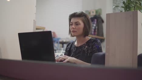 Young-business-woman-sitting-by-the-window-with-a-laptop-and-working