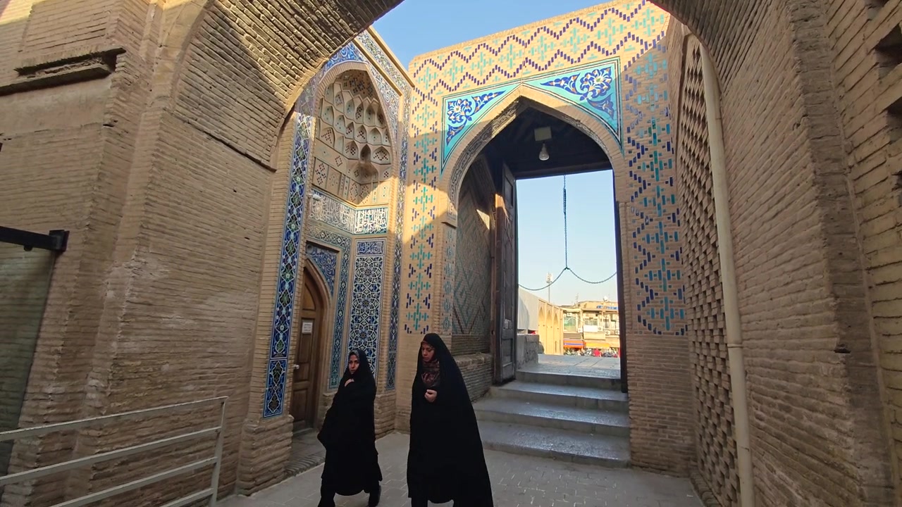 Duas mulheres de chador caminhando por um arco persa histórico.