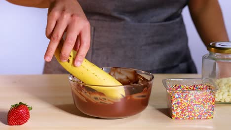 banana dipped in chocolate with sprinkles nearby