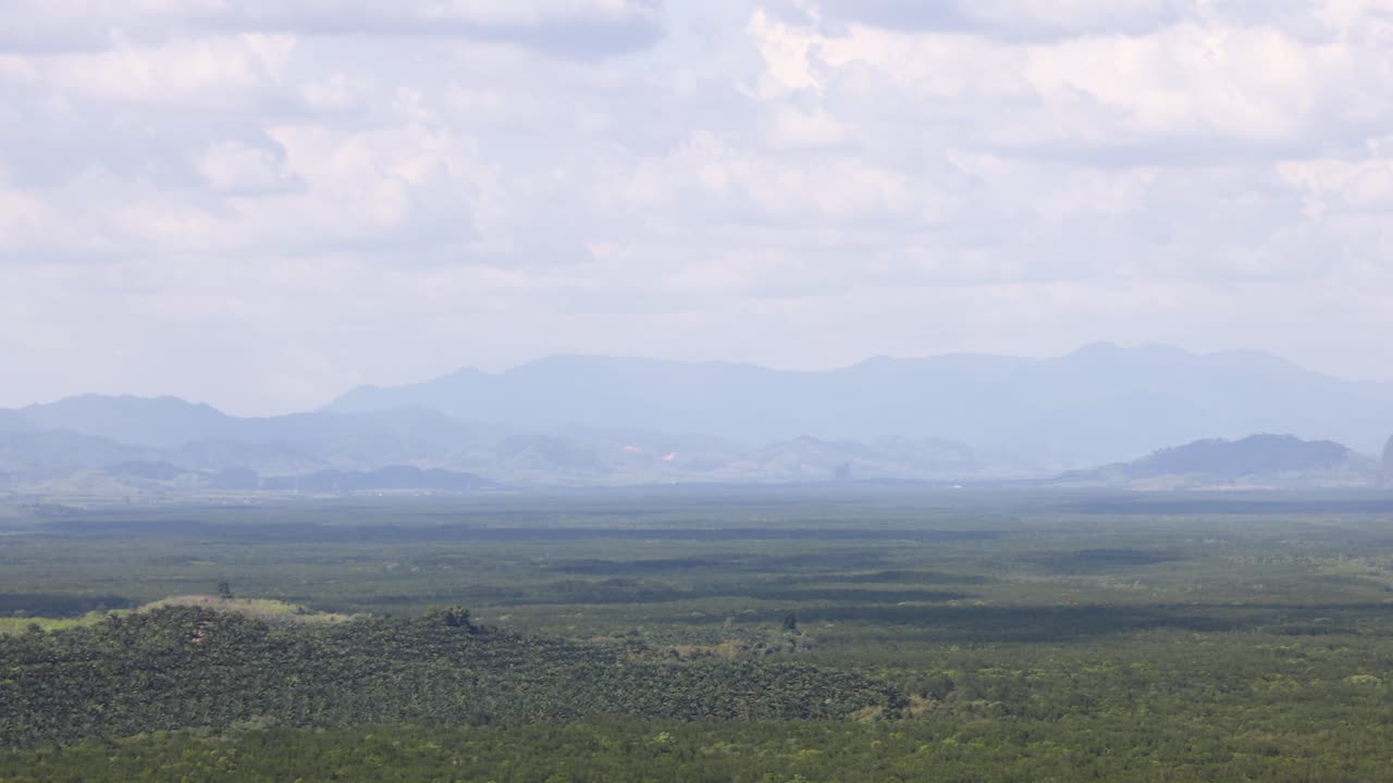 Expansive view of Phang Nga's green hills and distant limestone formations under a bright, cloudy sky