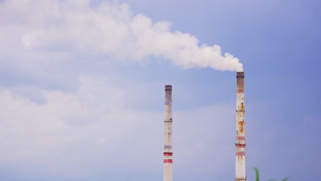 plant pipes producing white smoke into air. industrial smoke polluting atmosphere. blue sky backdrop.