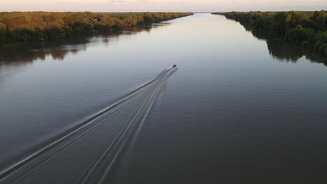 aerial tracking shot of cruising speed boat on calm amazon river during epic sunset