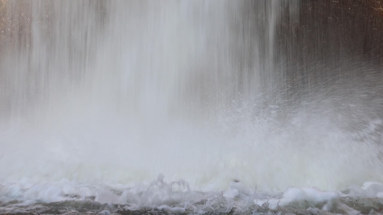 Close-up of waterfall pouring onto rocks, creating mist and turbulence, natural daylight, steady camera