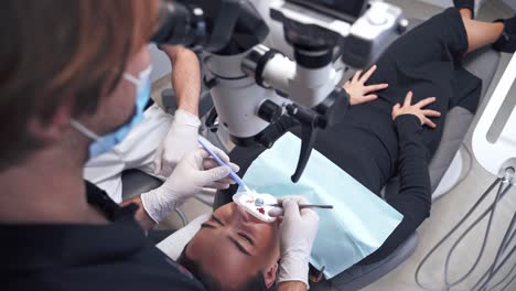 young woman laying in the dental chair. dentist treating patient's teeth in the dental office. stomatologist examines teeth through the microscope.