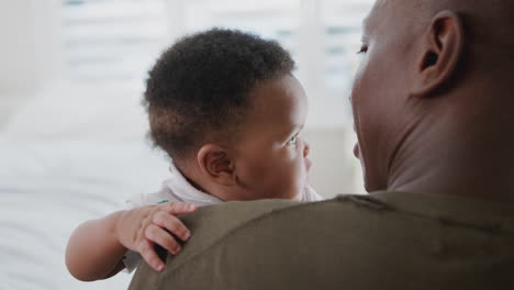 over the shoulder view of father cuddling and playing with baby son in nursery at home