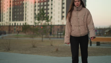 front shot of a young girl in a peach jacket and black trousers is captured rollerblading along a paved path in a serene park. highlights her focused expression as she enjoys the outdoor activity