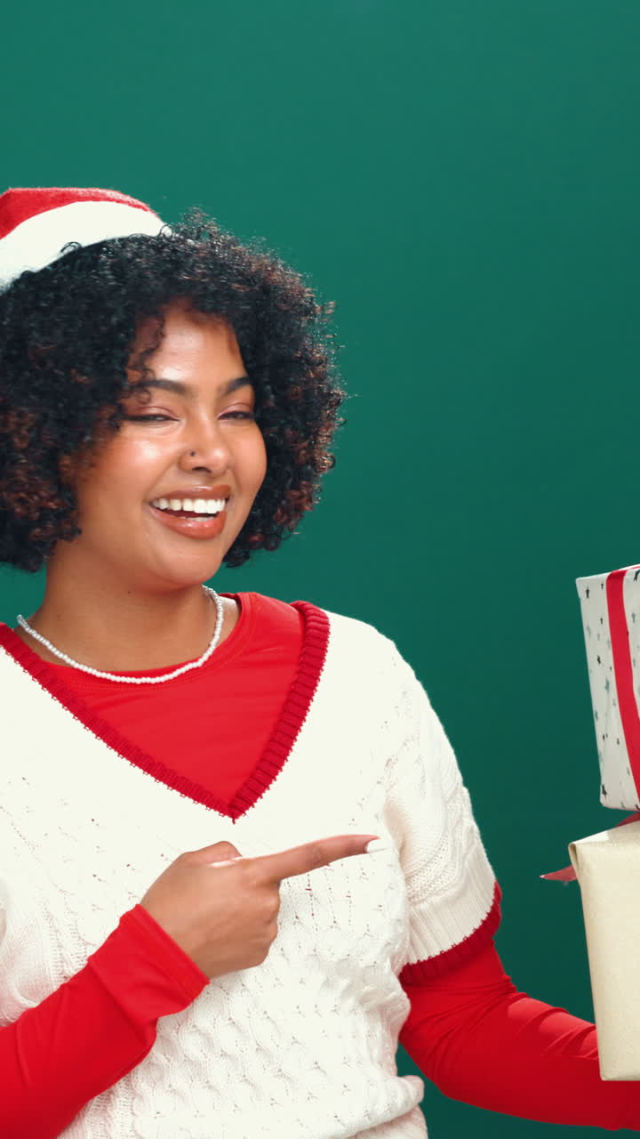 Happy Young Woman in Santa Hat Pointing at Christmas Gifts