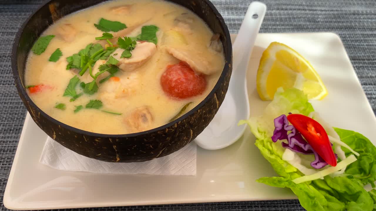 sopa de coco tailandesa picante con pollo y verduras en un tazón de coco, plato caliente en el restaurante de cocina tailandesa, 4k inclinando hacia arriba