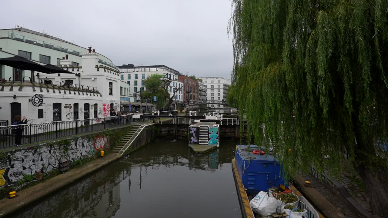 Tourists explore Camden Town canal near a dam with weeping willow trees and graffiti-covered walls