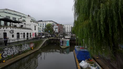 tourists explore camden town canal near a dam with weeping willow trees and graffiti-covered walls
