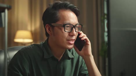 close up asian man talking on mobile phone while works on personal computer and 3d printer in home office, he works at night