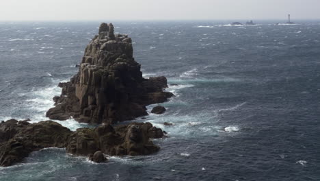 Wellen-Schlagen-Gegen-Felsen-Am-Landende,-In-Der-Ferne-Ist-Der-Leuchtturm-Eines-Langschiffs-Zu-Sehen