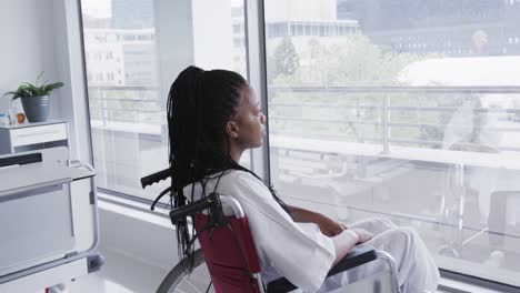 Paciente-Afroamericana-En-Silla-De-Ruedas-Mirando-Por-La-Ventana-En-La-Habitación-Del-Hospital,-Cámara-Lenta