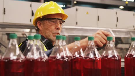 Worker-checking-juice-bottles-on-production-line