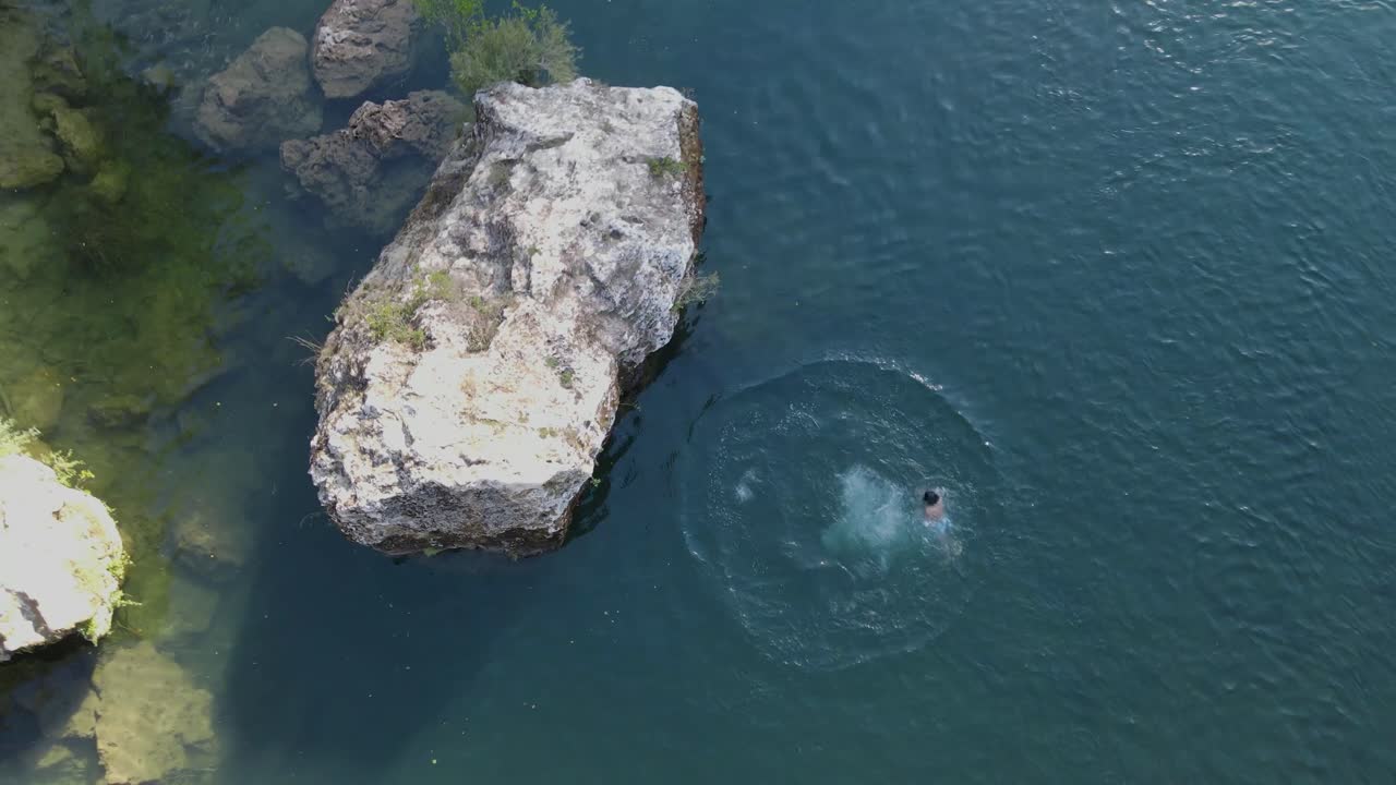 Drone flying away from a person swimming in a deep blue water. Person swimming fast in deep water with camera flying away and revealing a large blue river. Aerial cinematic shot of a person swimming