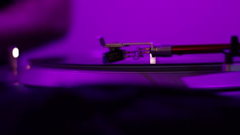 A-Vintage-Record-Player-Needle-spins-a-warped-and-distorted-record-under-a-black-light-while-a-Disk-Jockey-DJ-adjusts-the-speed-from-slow-to-fast