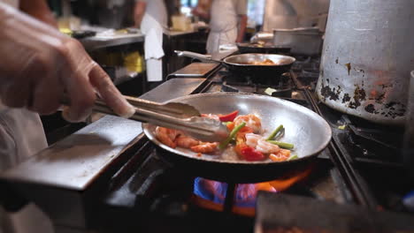 chef pan fries shrimp and vegetables, cook uses tongs to move around vegetables and shrimp in pan, slow motion hd