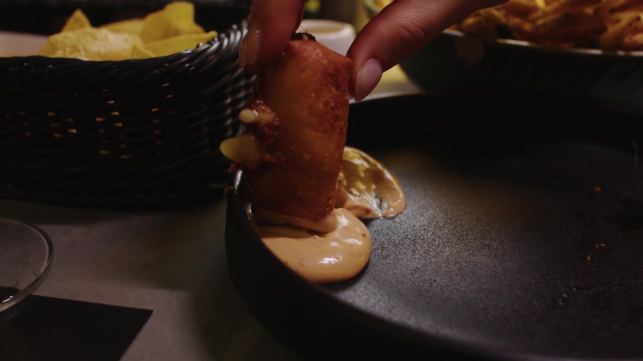 Hand dipping fried food into sauce on a black plate at a restaurant table setting