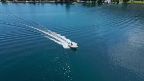 Tracking-shot-aerial-of-motorboat-speeding-on-peaceful-calm-lake-in-Pella,-Italy