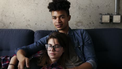 cute happy couple of young hipsters lying on the couch, laughing while watchingsomething on tv. leisure time, enjoying youth, living together. relationship goals.