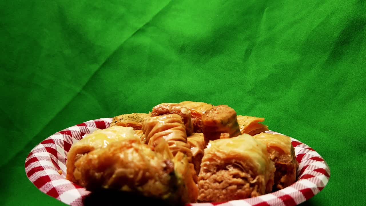 4k Loop3-3 Baklava dessert assorted variation of bite sized sweets rotating 120 degree plate with green screen back drop on a checked picnic style paper plate in red and white