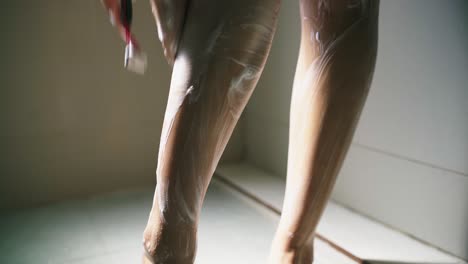 젊은 여성이 아침에 샤워를 하고 거품과 면도기로 다리를 면도하는 근접 촬영