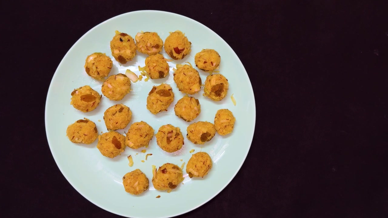 Ladoo al cocco fatto in casa con mandorle e uvetta servito su un piatto blu.