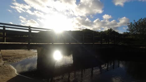 Sonnenuntergang-Zeitraffer-Wolken-Gespiegelt-Unter-Holzbrücke-Fließenden-Strandbach