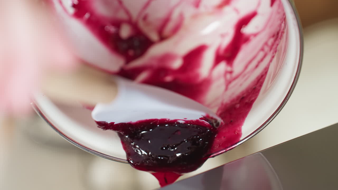 Close up of thick blended berry puree being poured from white bowl with spatula into background container, rich dark red texture flowing smoothly, perfect for dessert and smoothie