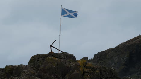 The-National-Flag-of-Scotland-also-known-as-the-Saltire-and-St-Andrew's-Cross-flies-in-a-stiff-breeze-on-top-of-rocks-in-the-coastal-village-of-Port-Patrick-in-Dumfries-and-Galloway,-Scotland