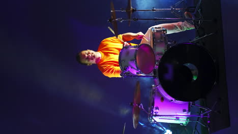 a man playing drums on a gloomy stage. neon lighting. vertical video.