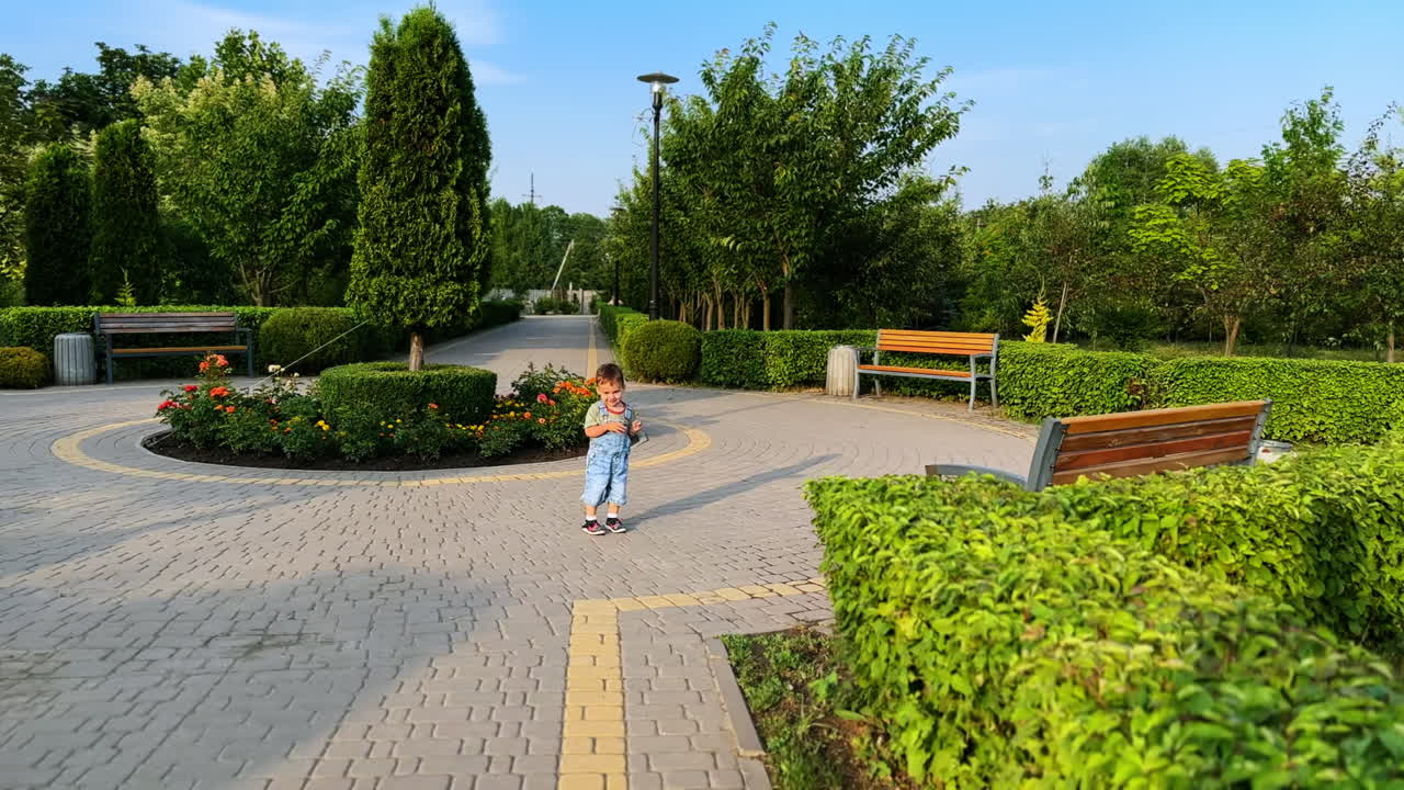 Catching up with a happy cute toddler boy running by the park. Active smiling kid is on the walk on sunny day.