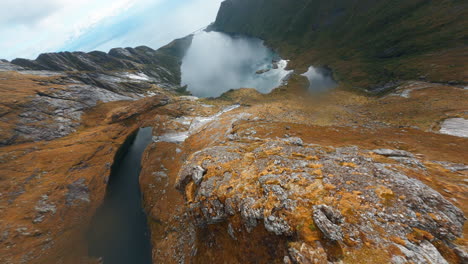 Diving-a-mountain-crest-of-Reinebringen-with-gorgeous-lakes-in-the-background,-Cinematic-FPV-drone,-Lofoten-Islands-in-Norway